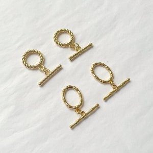 Op de afbeelding: Drie goudkleurige metalen schuifgespen met een gedraaid touwontwerp en een rechte stang. De gespen bevinden zich op een witte achtergrond.