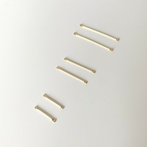 May include: Six gold-coloured metal connector bars with loops on each end. The bars are arranged in a staggered pattern on a white surface.