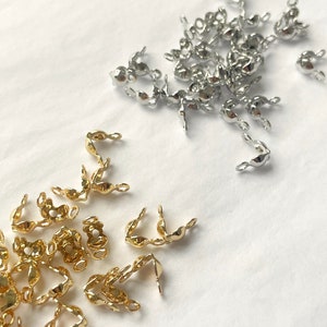 May include: A collection of gold and silver metal crimp beads. The beads are small and have a rounded shape with a loop on each end. They are used for jewellery making.