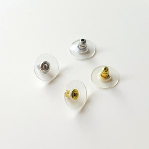 May include: Four clear plastic earring backs with different coloured metal posts. The posts are silver, gold, and two gold.