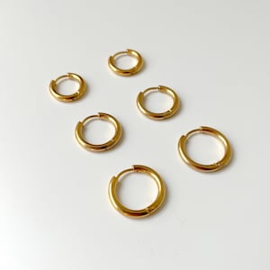 May include: Five gold hoop earrings of different sizes on a white background.