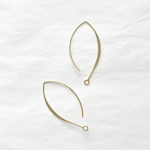 May include: A pair of gold-toned leaf-shaped earrings with a simple design. The earrings are made of thin metal and have a delicate, minimalist look.