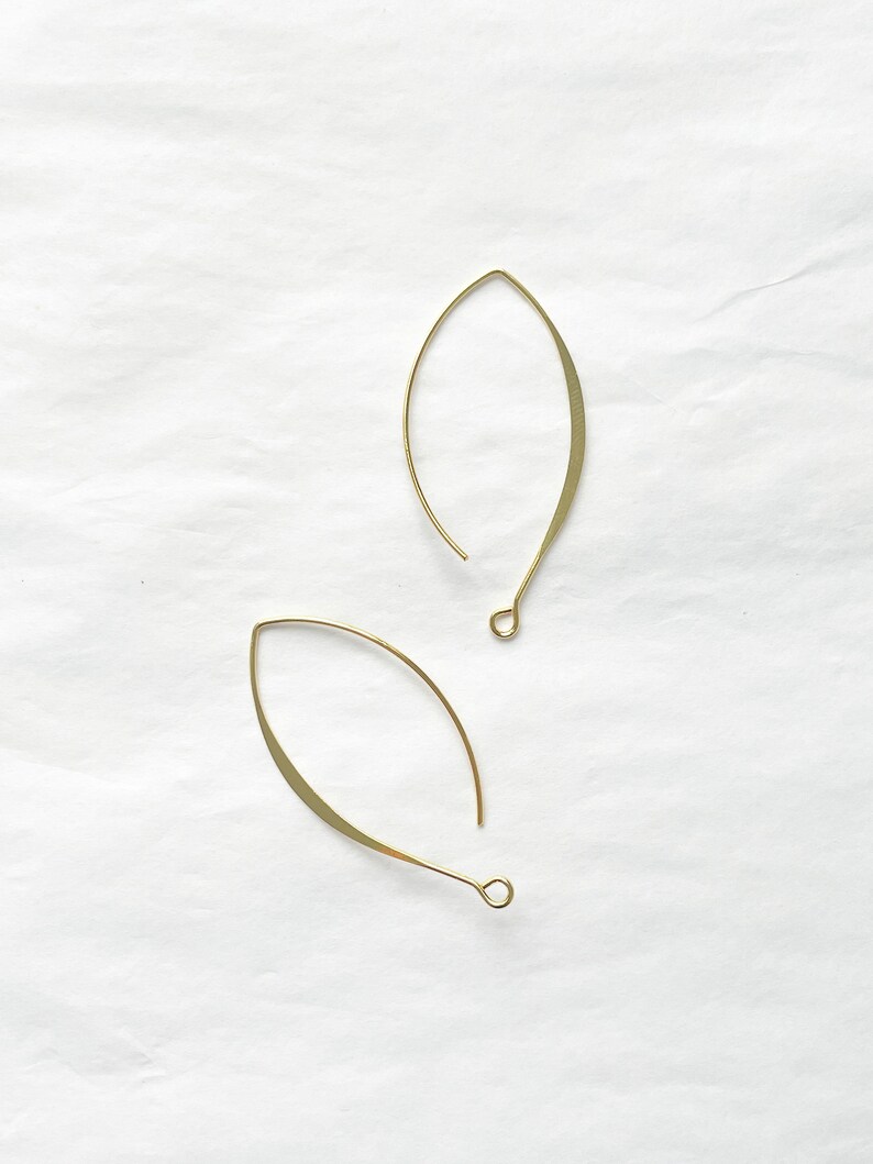 May include: A pair of gold-toned leaf-shaped earrings with a simple design. The earrings are made of thin metal and have a delicate, minimalist look.