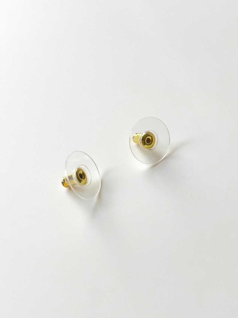 K&ouml;nnte beinhalten: Zwei transparente Ohrstecker aus Kunststoff mit goldenen Metallstiften. Die R&auml;nder sind rund und haben eine glatte Oberfl&auml;che.