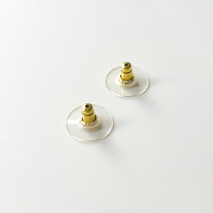 K&ouml;nnte beinhalten: Zwei transparente Ohrstecker aus Kunststoff mit goldenen Metallstiften. Die R&auml;nder sind rund und haben einen leichten Rand.