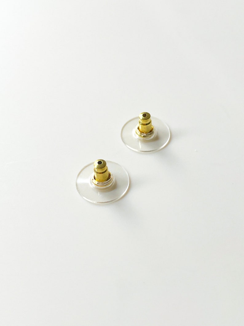 K&ouml;nnte beinhalten: Zwei transparente Ohrstecker aus Kunststoff mit goldenen Metallstiften. Die R&auml;nder sind rund und haben einen leichten Rand.