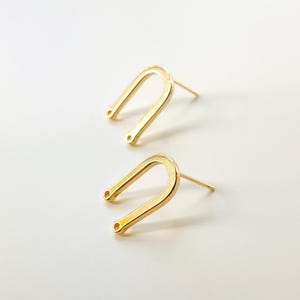 Op de afbeelding: Een paar gouden oorringen in de vorm van een hoefijzer met een klein gaatje aan elke kant.