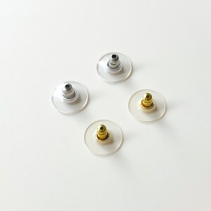 K&ouml;nnte beinhalten: Vier Ohrstecker in verschiedenen Farben: Silber, Gold und zwei weitere Silber. Die Stecker sind aus klarem Kunststoff mit einem Metallstift.