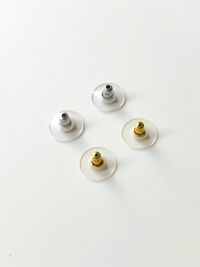 K&ouml;nnte beinhalten: Vier Ohrstecker in verschiedenen Farben: Silber, Gold und zwei weitere Silber. Die Stecker sind aus klarem Kunststoff mit einem Metallstift.