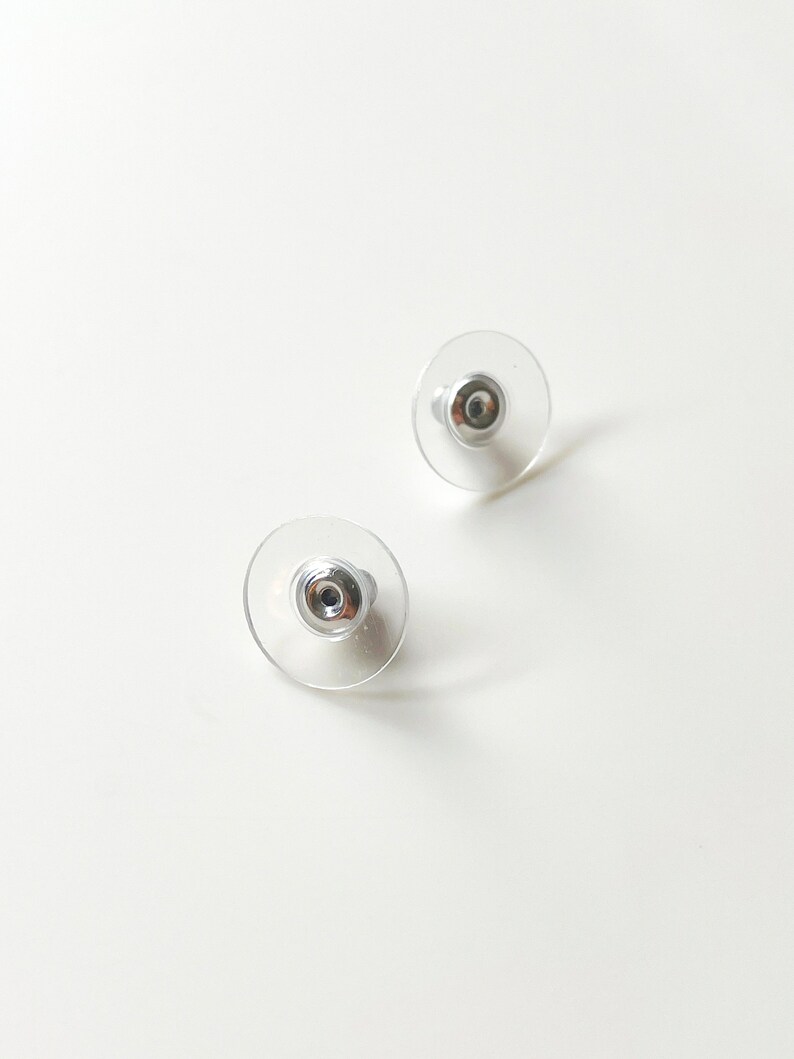 K&ouml;nnte beinhalten: Ein Paar durchsichtige Ohrstecker aus Kunststoff mit silbernen Metallstiften.