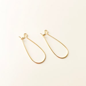 May include: A pair of gold teardrop-shaped hoop earrings. The earrings are made of thin wire and have a simple, elegant design.