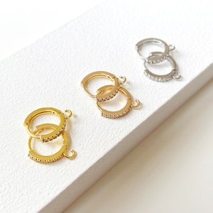 Może przedstawiać: Trzy pary kolczyków koła z pavé z przezroczystych cyrkonii. Kolczyki są dostępne w kolorze złotym, srebrnym i różowym złocie.