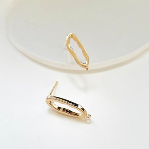 Può includere: Due fermagli per orecchini dorati con un anello a un'estremità e un perno all'altra. I fermagli hanno una forma ovale con un bordo irregolare.