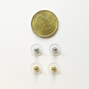 K&ouml;nnte beinhalten: Vier Ohrstecker-R&uuml;ckstecker, zwei silberne und zwei goldene, auf wei&szlig;em Hintergrund. Die Ohrstecker-R&uuml;ckstecker sind in zwei Reihen zu je zwei angeordnet, wobei die silbernen oben und die goldenen unten liegen.