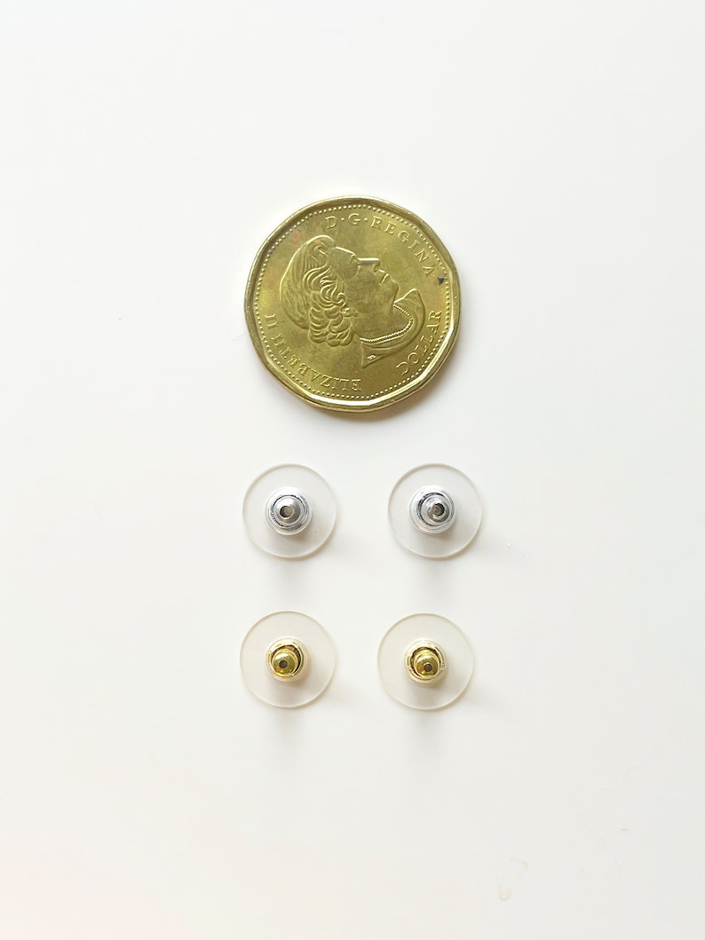 K&ouml;nnte beinhalten: Vier Ohrstecker-R&uuml;ckstecker, zwei silberne und zwei goldene, auf wei&szlig;em Hintergrund. Die Ohrstecker-R&uuml;ckstecker sind in zwei Reihen zu je zwei angeordnet, wobei die silbernen oben und die goldenen unten liegen.