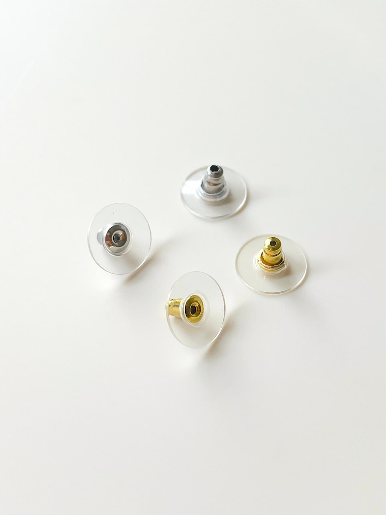 K&ouml;nnte beinhalten: Vier transparente Ohrstecker aus Kunststoff mit unterschiedlichfarbigen Metallstiften. Die Stifte sind silber, gold und zwei gold.