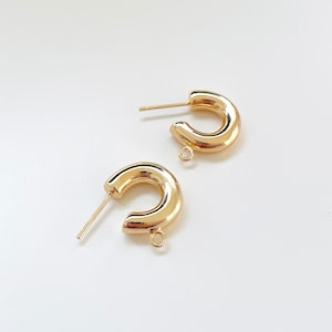 May include: A pair of gold hoop earrings with a thick, rounded design. The earrings have a simple, minimalist style.