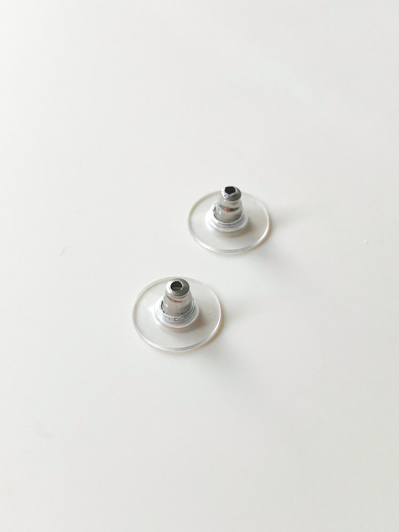 K&ouml;nnte beinhalten: Zwei transparente Ohrstecker aus Kunststoff mit einem silbernen Metallstift.
