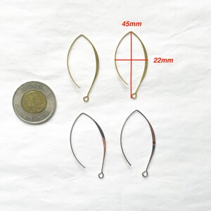 May include: Four gold-toned earring wires, two are 4.5 cm long and 2.2 cm wide, and two are smaller. The earring wires are on a white surface.