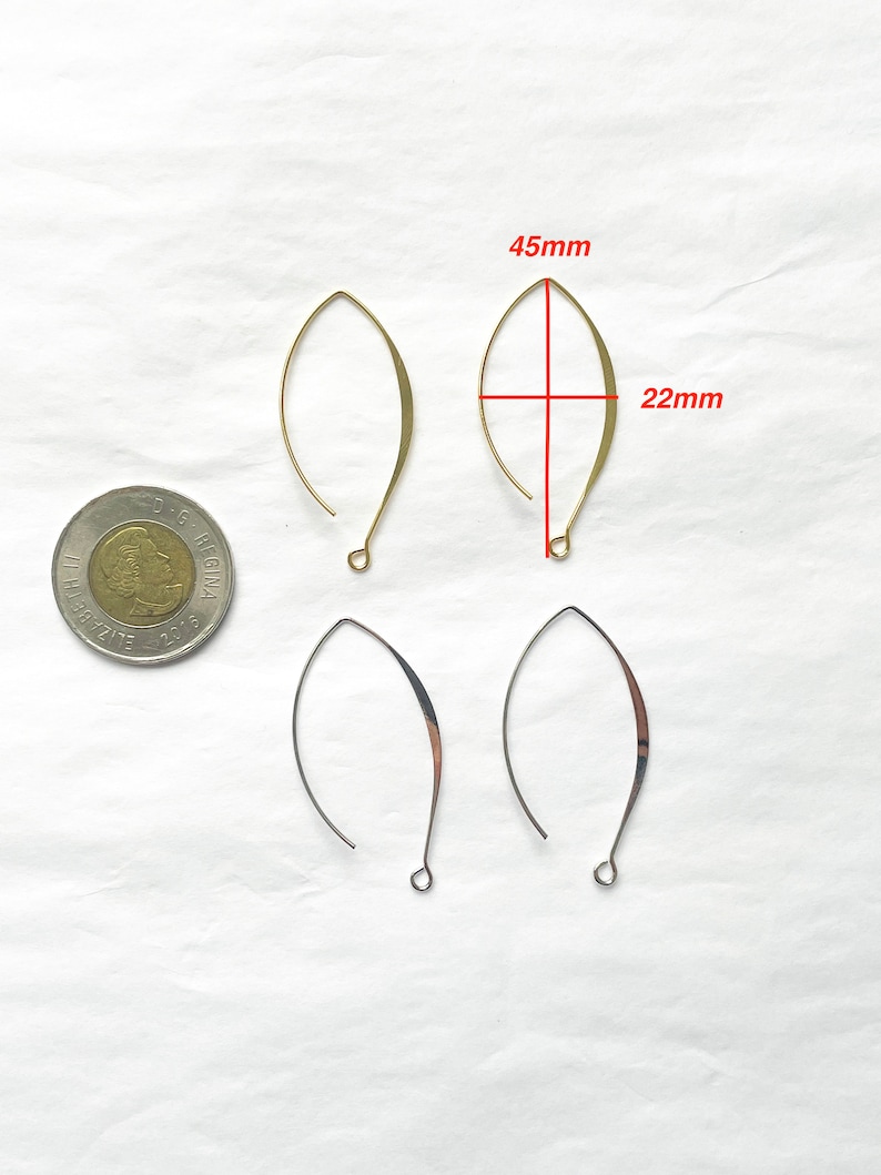 May include: Four gold-toned earring wires, two are 4.5 cm long and 2.2 cm wide, and two are smaller. The earring wires are on a white surface.