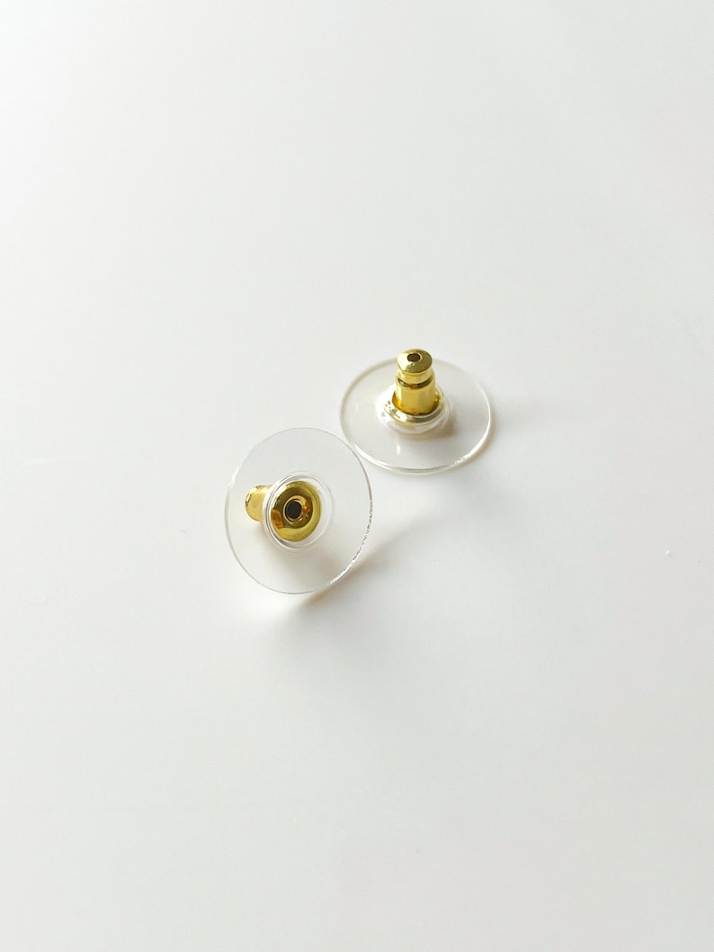 K&ouml;nnte beinhalten: Zwei transparente Ohrstecker aus Kunststoff mit goldenen Metallstiften. Die R&auml;nder sind rund und haben ein kleines Loch in der Mitte.