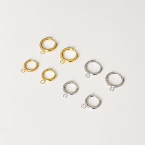 May include: A selection of gold and silver hoop earrings. The earrings are displayed on a white background. The gold earrings have a polished appearance, while the silver ones have a matte finish. Each earring features a small loop at the base.