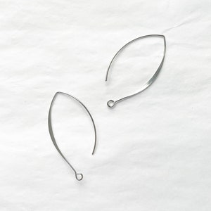 May include: A pair of silver-toned, open hoop earrings with a slightly curved, leaf-shaped design.