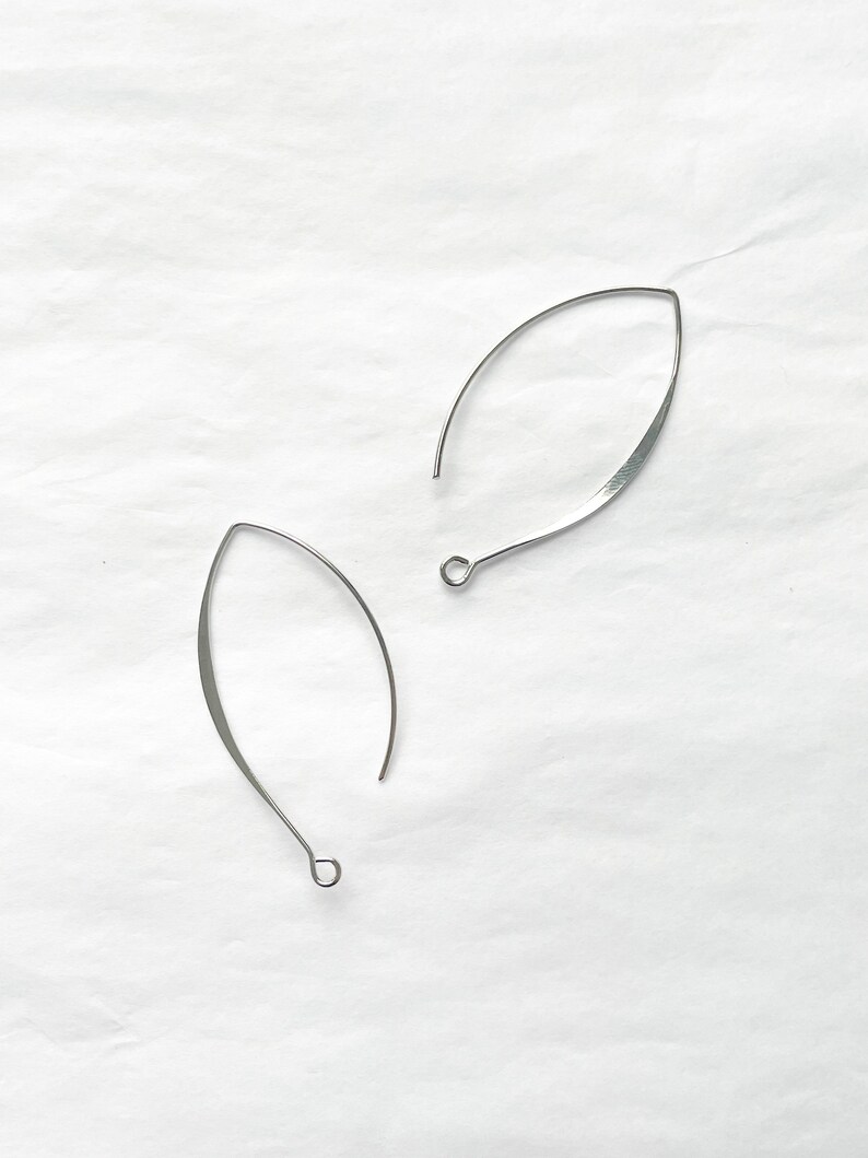 May include: A pair of silver-toned, open hoop earrings with a slightly curved, leaf-shaped design.