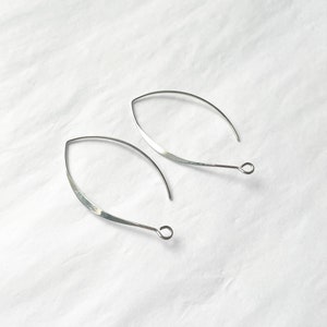 May include: A pair of silver, open hoop earrings with a slightly curved, teardrop shape. The earrings have a simple, minimalist design.
