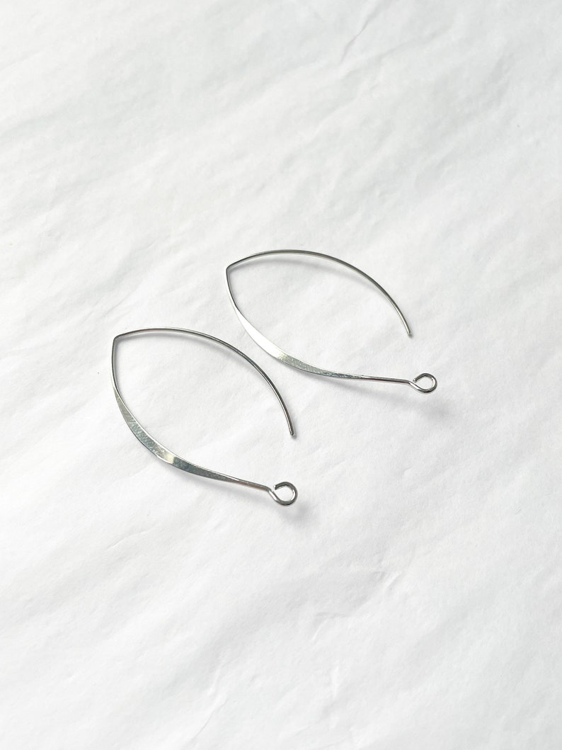 May include: A pair of silver, open hoop earrings with a slightly curved, teardrop shape. The earrings have a simple, minimalist design.