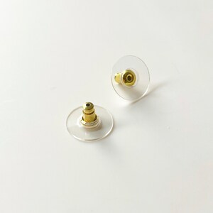 K&ouml;nnte beinhalten: Zwei transparente Ohrstecker aus Kunststoff mit goldenen Metallstiften. Die R&auml;nder sind rund und leicht erh&ouml;ht.