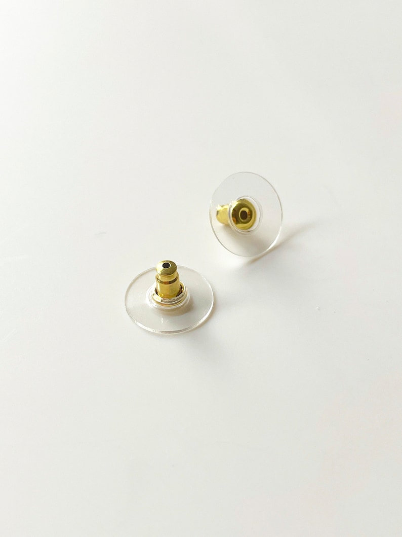 K&ouml;nnte beinhalten: Zwei transparente Ohrstecker aus Kunststoff mit goldenen Metallstiften. Die R&auml;nder sind rund und leicht erh&ouml;ht.
