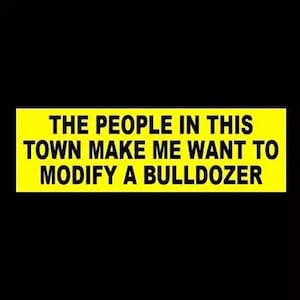 May include: Yellow bumper sticker with black text that reads "The people in this town make me want to modify a bulldozer."