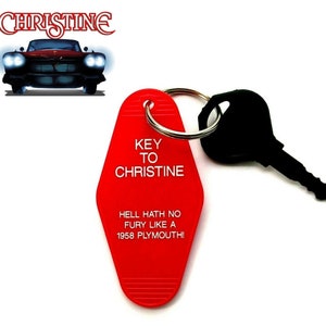 May include: Red motel key chain with the text "KEY TO CHRISTINE" and "HELL HATH NO FURY LIKE A 1958 PLYMOUTH!"  The keychain has a silver ring and a black key attached.
