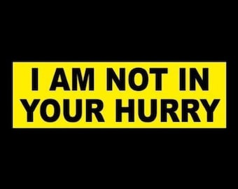 May include: Yellow bumper sticker with black text that reads "I AM NOT IN YOUR HURRY".