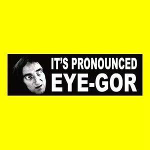 May include: A black and white image of a man's face with the text "IT'S PRONOUNCED EYE-GOR" in white letters on a black rectangle. The background is bright yellow.