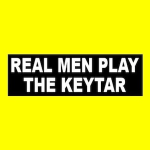 May include: Black and white rectangular sign with the text "REAL MEN PLAY THE KEYTAR" in white letters.