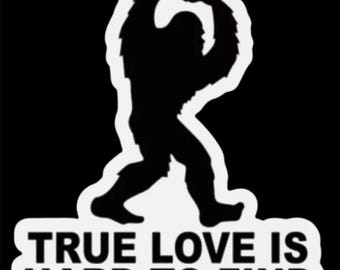 May include: A black silhouette of a Bigfoot holding a red heart in its hands. The text "TRUE LOVE IS HARD TO FIND" is below the image.
