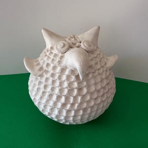 Peut inclure: Sculpture de hibou blanc cassé. Le corps du hibou est texturé, avec de grands yeux et des oreilles pointues. La sculpture est faite d'un matériau clair et est posée sur une surface verte. Objet décoratif fait à la main.