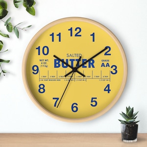 May include: A round wall clock with a yellow face and a wooden frame. The clock face features blue numerals and the word "BUTTER" in large blue letters. It also includes text indicating the net weight of 4 oz (113g).