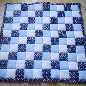 Könnte beinhalten: Eine blaue und weiße karierte Babydecke mit einem Halbmondmuster. Die Decke ist aus weichem, bequemem Stoff und perfekt zum Kuscheln.