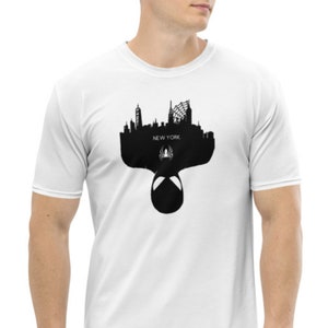 May include: White t-shirt featuring a black silhouette of the New York City skyline, a spider symbol, and the word "NEW YORK". The design includes the mask of a superhero. The shirt is made of a soft, comfortable material.