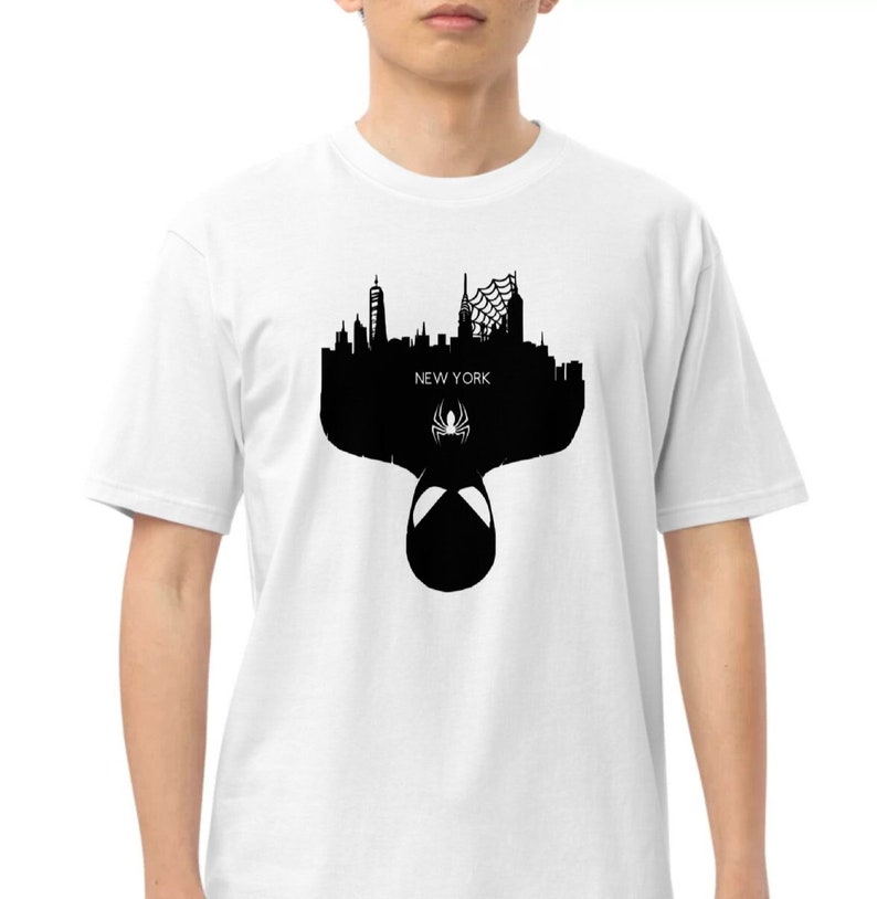May include: White t-shirt featuring a black silhouette of the New York City skyline, a spider symbol, and the text "NEW YORK". The design includes the Spider-Man mask.