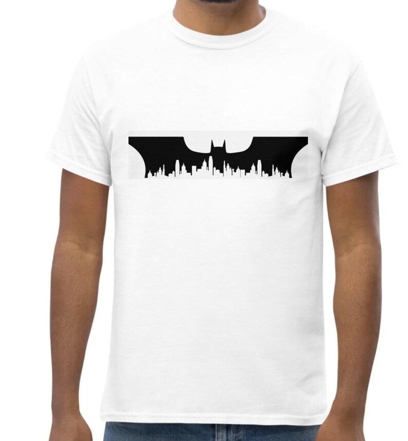May include: A white t-shirt featuring a black silhouette of the Batman logo, with a bat and a city skyline in the background.