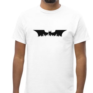 May include: A white t-shirt with a black Batman logo featuring a bat silhouette with a cityscape in the background.
