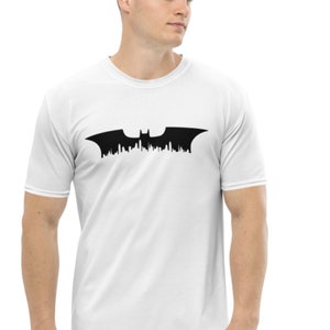 May include: White t-shirt featuring a black silhouette of the Batman logo, with a cityscape design.