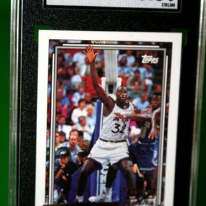 May include: A 1992-93 Topps Shaquille O'Neal Gold basketball card, number 362, graded 8.5 by SGC. The card features O'Neal in a white pinstriped Orlando Magic jersey with the number 32, reaching upward during a game with a crowd in the background.