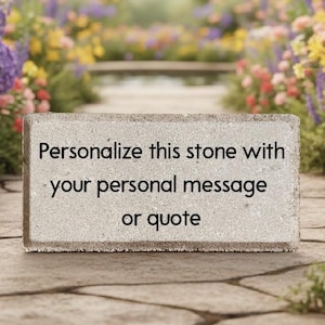 May include: A rectangular stone with the text "Personalize this stone with your personal message or quote" is set on a stone path. The background features a garden with colorful flowers and butterflies.