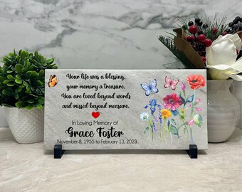 May include: A memorial plaque with a marble-like background features a floral design and butterflies. The text reads "Your life was a blessing... In Loving Memory of Grace Foster, November 8, 1955 to February 13, 2023."