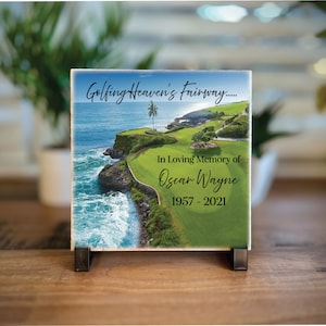 May include: A white ceramic tile with a scenic image of a golf course overlooking the ocean. The text "Golfing Heaven's Fairway..." is at the top of the tile. The text "In Loving Memory of Oscar Wayne 1957 - 2021" is in the center of the tile.